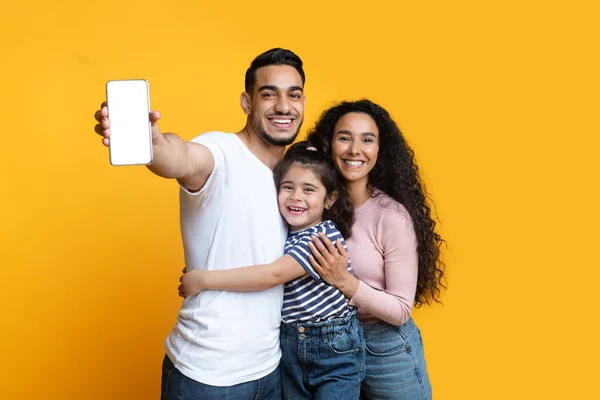 Família árabe alegre de três demonstrando Smartphone em branco com tela branca — Fotografia de Stock
