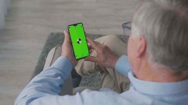 Vista por encima del hombro en la red madura hombre de pelo gris en el teléfono inteligente con pantalla de clave de croma verde, tiro de seguimiento — Vídeos de Stock