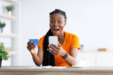 Modern cep telefonu ve kredi kartı tutan siyahi kadın, internette mal ve hizmetleri öderken evde kalıyor.