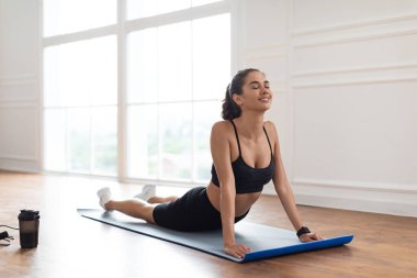 Genç bir kadın mindere geriliyor, kobra pozu.