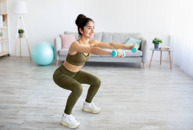 Güç egzersizi konsepti. Fit Hintli kadın evde dambıllarıyla çömeliyor, boş yer var.