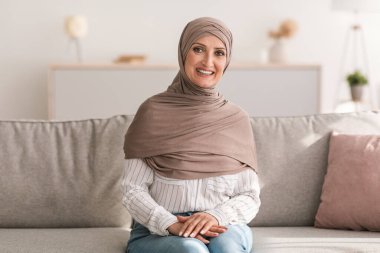 Neşeli kıdemli İslami Kadın Pozisyonu Evdeki Kameraya Gülümsüyor