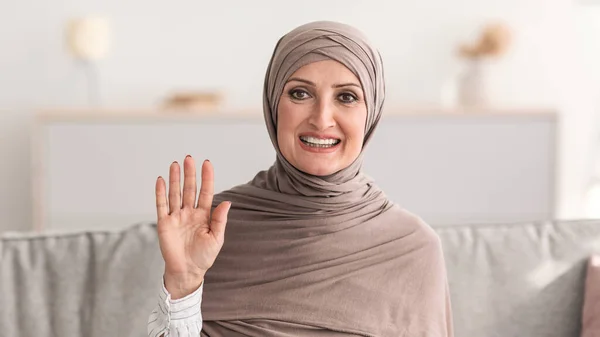 Allegro anziana donna in hijab onda mano seduta a casa — Foto Stock
