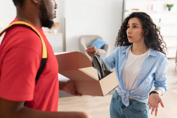 Verwirrte frustrierte Dame packt Karton aus, hält Kleidung in der Hand und beschwert sich — Stockfoto