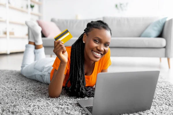 Mujer negra joven feliz usando el ordenador portátil y la tarjeta de crédito para comprar bienes a la venta, transferir dinero o utilizar los servicios bancarios —  Fotos de Stock