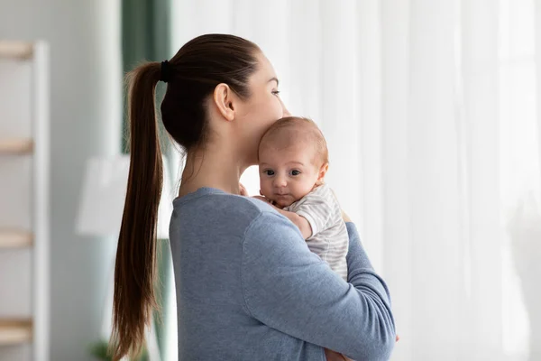 Mödrars psykiska hälsoproblem. Ung kvinna som håller nyfödda barn stående nära fönstret — Stockfoto