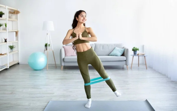 Full length of charming Indian woman doing exercises with elastic band during home workout — Stock Photo, Image