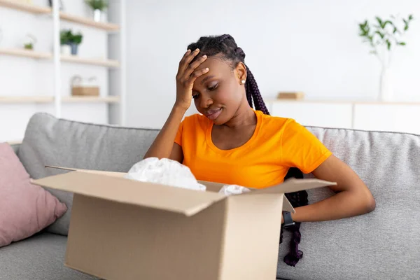 Enttäuschte schwarze Frau, die ihre Lieferung auspackt, in die falsche Schachtel schaut und frustriert ihre Stirn berührt — Stockfoto