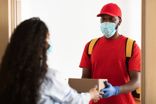 Black delivery man in mask giving box to female client — Stock Photo, Image