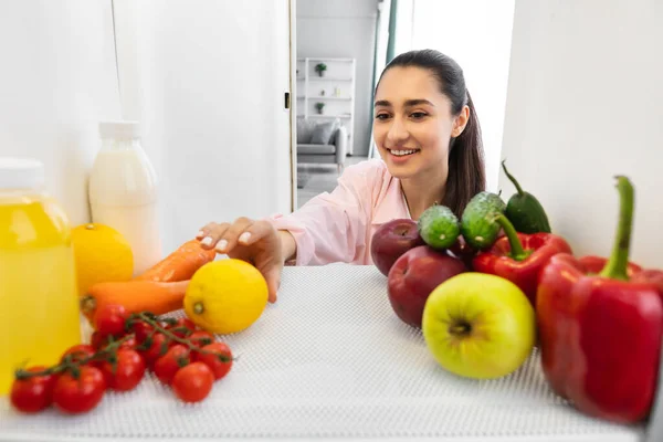 Femme arabe souriante ouvrant le réfrigérateur et prenant des aliments frais — Photo