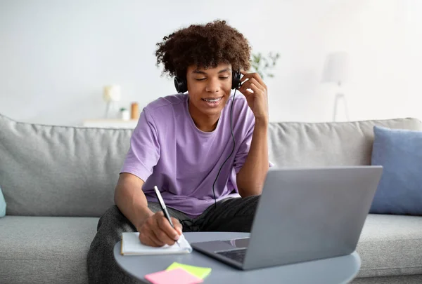Educação baseada na Web. Estudante adolescente inteligente em fones de ouvido tomando notas durante o seminário on-line no laptop em casa — Fotografia de Stock