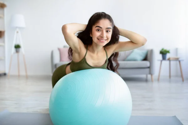 Felice giovane donna indiana facendo esercizi con palla fitness, rafforzando i muscoli della schiena a casa — Foto Stock