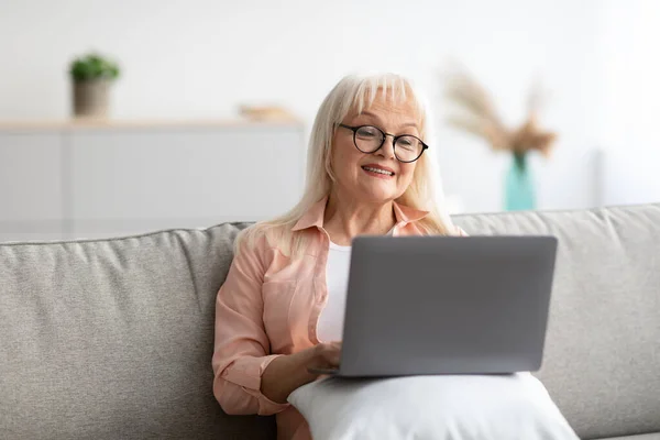 Volwassen vrouw zitten op de bank en met behulp van computer — Stockfoto