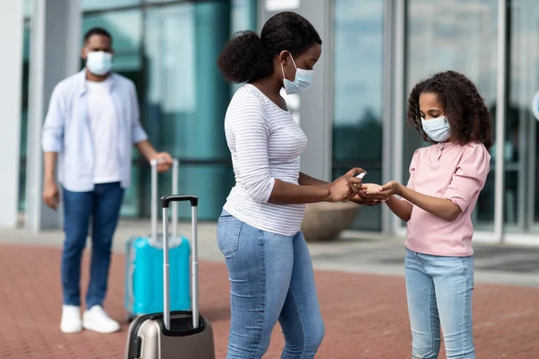 Negro familia viajando, mamá usando desinfectante en hijas manos —  Fotos de Stock