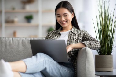 Laptop klavyesinde yazan neşeli Asyalı kadın, ev içi.