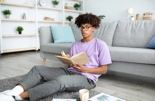 Focado livro de leitura adolescente preto, sentado no chão, estudando em casa — Fotografia de Stock