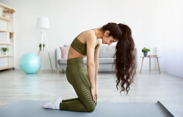 Seitenansicht einer jungen, fitten Inderin, die Rückenbeuge macht und zu Hause Übungen für ihre Wirbelsäule macht, in voller Länge — Stockfoto