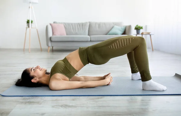 Vista lateral de la señora india haciendo ejercicio abdominales, de pie en medio puente postura de yoga durante su entrenamiento doméstico — Foto de Stock