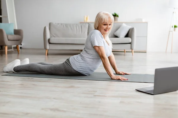 Senior woman stretching back on mat with pc — Stock Photo, Image