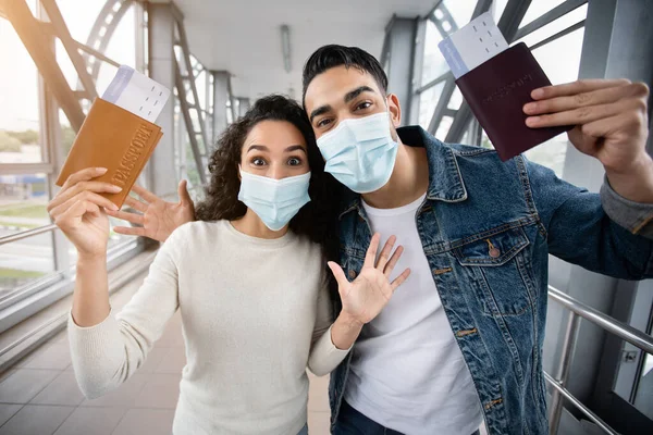 Vacaciones Finalmente. Pareja emocionada usando máscaras en el aeropuerto sosteniendo pasaportes y boletos —  Fotos de Stock