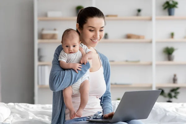 Freelance et maternité. Maman travaillant sur ordinateur portable à la maison et tenant bébé — Photo