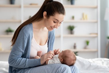 Neşeli, genç, sevgi dolu anne evde sevimli bebeğiyle oynuyor.