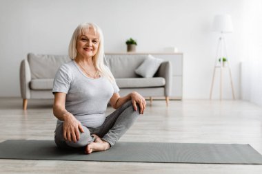 Evde yoga minderiyle egzersiz yapan olgun bir kadın.