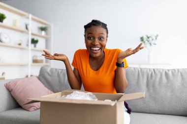 Heyecanlı siyah kadın paketini alıyor, karton kutusunu açıyor, büyük alışverişlerden memnun.