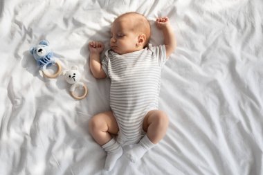 Yatakta çıngıraklı oyuncaklarla kestirip duran sevimli bebek portresi.