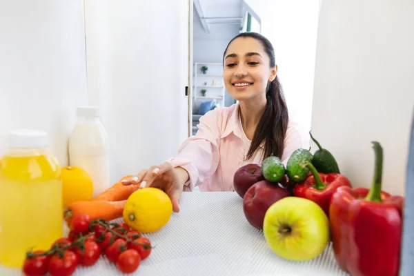 Femme souriante ouvrant le réfrigérateur et prenant des aliments frais — Photo