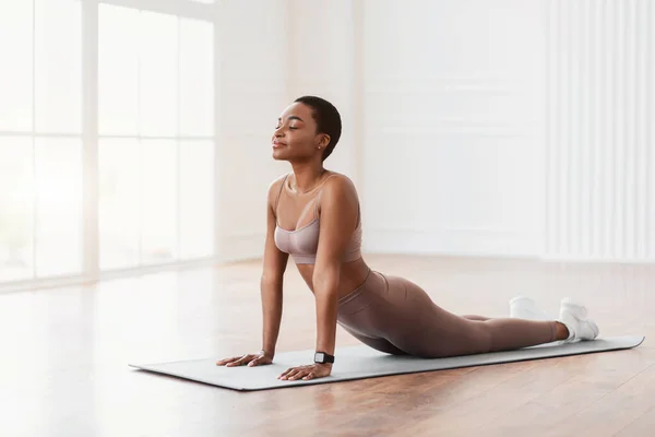 Fit young black woman practicing yoga on sports mat at home