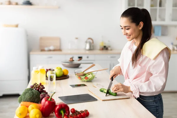 Kvinna matlagning sallad och använda tablett i köket — Stockfoto