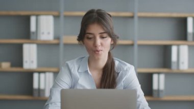 Ofiste dizüstü bilgisayarda çalışan genç bayan ofis çalışanı başarılı sonuçlar okuyor ya da rapor veriyor ve gülümsüyor.