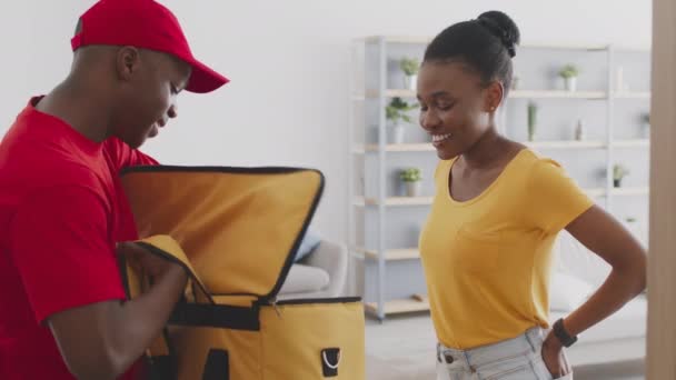 Serviço de entrega em domicílio. mensageiro masculino preto levando caixa fora do saco e dando ordem para senhora afro-americana positiva — Vídeo de Stock