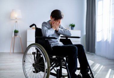 Engelli gençlerde depresyon. Tekerlekli sandalyedeki mutsuz engelli çocuk evde ağlıyor.