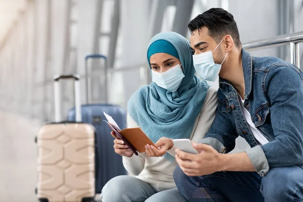 Pareja musulmana en máscaras médicas esperando el vuelo en la terminal del aeropuerto —  Fotos de Stock