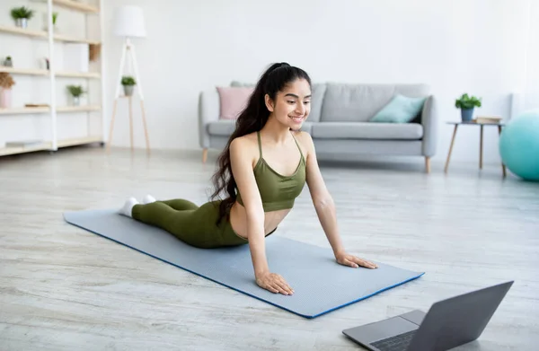 Volledige lengte van jonge Indiase vrouw doet cobra asana, training om online yoga video op laptop thuis — Stockfoto