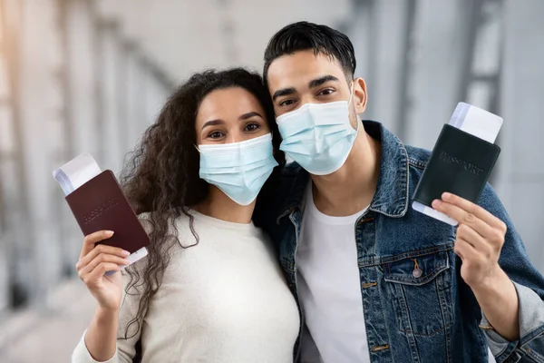 Joven pareja árabe con máscaras médicas en el aeropuerto sosteniendo pasaportes y boletos —  Fotos de Stock