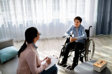Başarılı psikoterapi. Tekerlekli sandalyedeki mutlu çocuk başarısını ofisteki psikologla paylaşıyor.