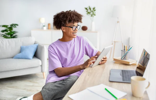 Webbbaserad skolgång. Positiv svart tonåring med hjälp av surfplatta och bärbar dator för online-utbildning hemma — Stockfoto