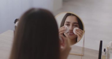 Orta Doğulu bir kadının aynadaki yansıması. Yüzünü losyon ve pamuk pedlerle temizliyor.