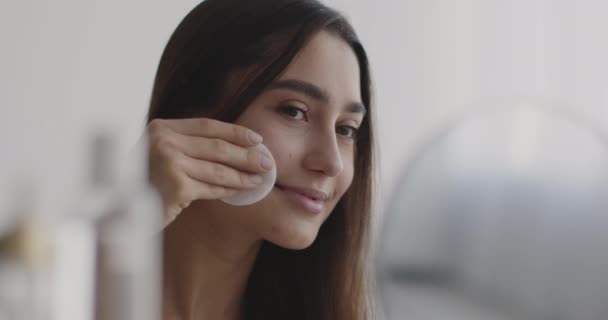 Make-up verwijderen en huid hydraterende. Jonge mooie oosterse vrouw reinigen gezicht met katoen pad, kijken naar spiegel — Stockvideo