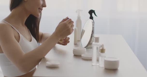 Jonge oosterse vrouw aanbrengen serum op gezicht, genieten van schoonheid procedures thuis, zitten aan boudoir tafel, zijaanzicht — Stockvideo