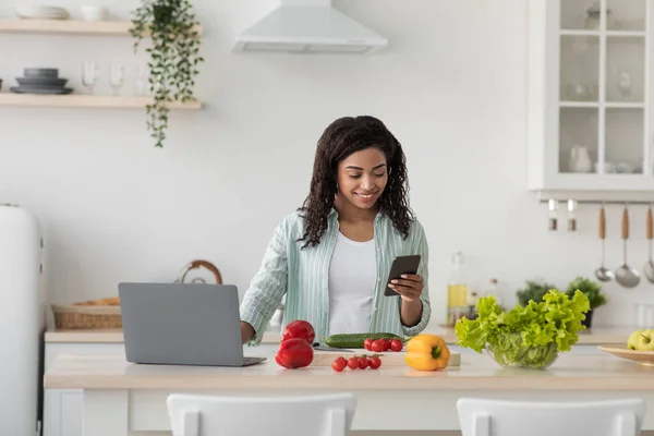 Woman in kitchen near paper bag full of fresh food and uses smartphone app to deliver from supermarket — Stock Photo, Image