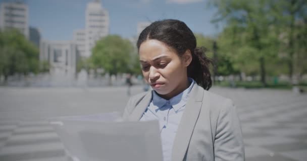 Problems with document flow. Disturbed african american lady reading papers outdoors, found mistakes, tracking shot — Stock Video