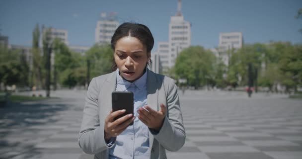 ビジネス危機だ。アフリカ系アメリカ人の女性がスマートフォンで電子メールを読んで不幸な気分になり、屋外を歩く — ストック動画