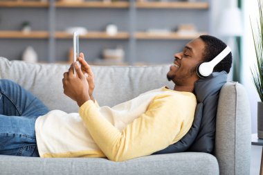 Rahat siyah adam kanepede uzanıyor, pedde film seyrediyor.