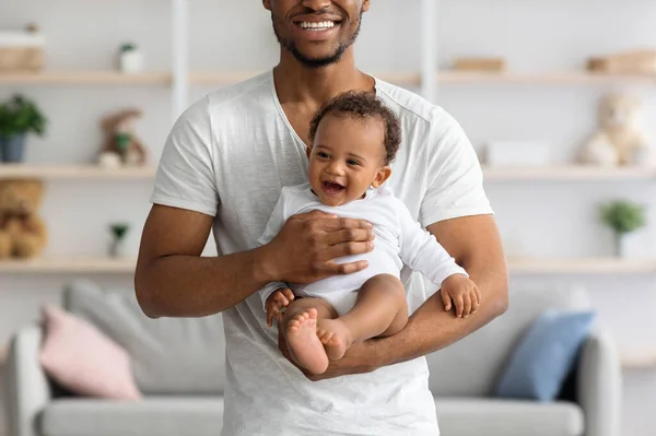 Lächelnder junger schwarzer Mann mit Neugeborenem in den Händen posiert zu Hause — Stockfoto
