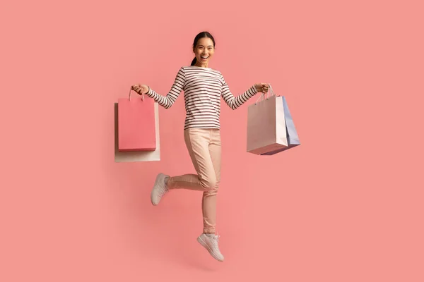 Акции в магазинах. Радостная молодая азиатка, прыгающая с пакетами из разноцветной бумаги — стоковое фото