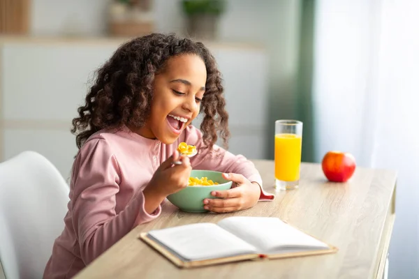 Linda chica adolescente negro que tiene desayuno saludable y libro de lectura mientras está sentado en el escritorio en casa — Foto de Stock